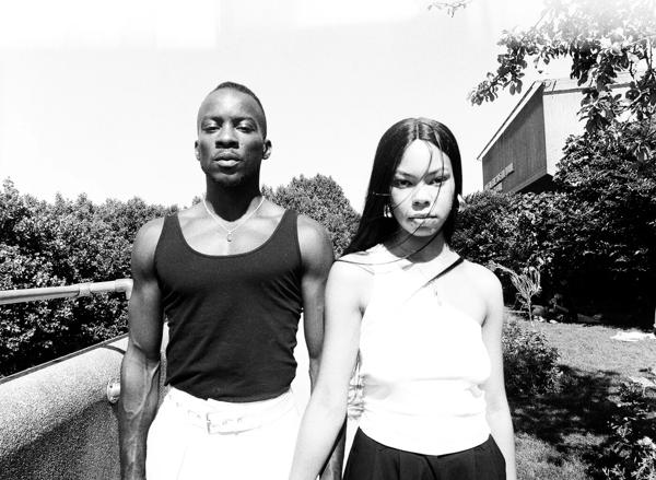 A black and white image of a Black man and Black woman standing side by side outdoors facing the camera