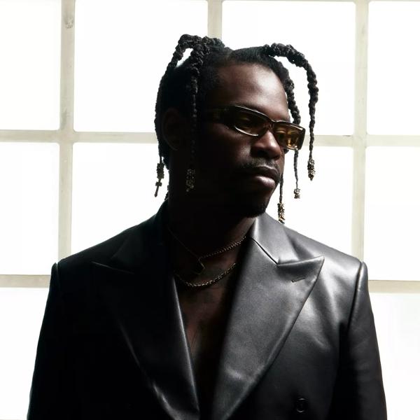 GAIKA stands in front of a light background, he wears a black leather jacket and sunglasses