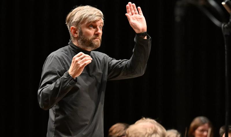 Conductor Kirill Karabits wearing a black outfit with this hand raised