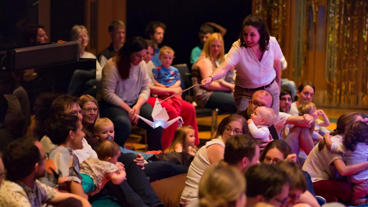 Performer floats a paper bird over a member of the audience full of babies and parents. 