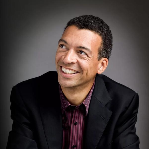 Baritone Roderick Williams in a black jacket and purple shirt smiling and looking in the distance 