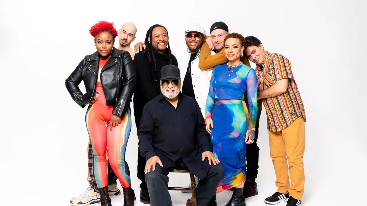 Members of Incognito standing and sitting together against a white background wearing different outfits.