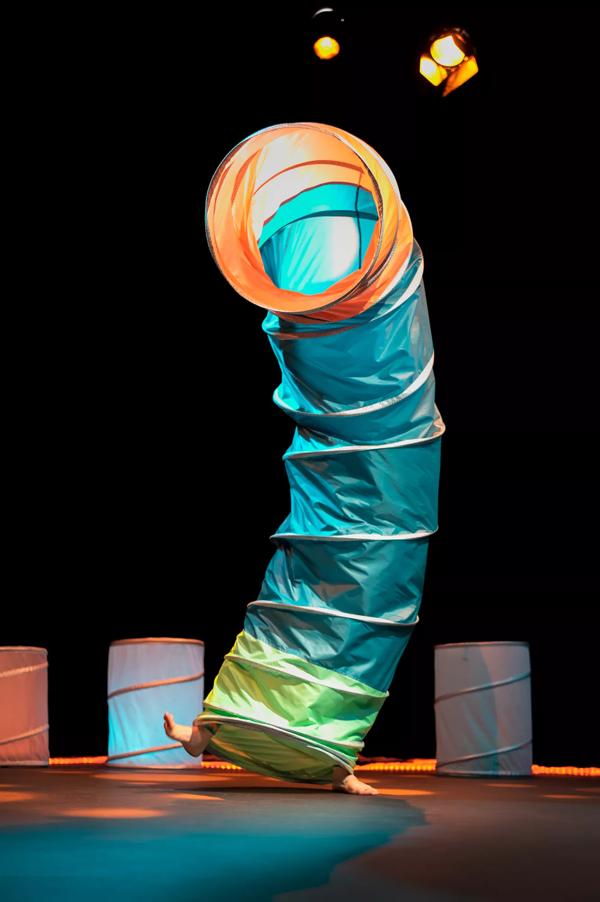 Actor on stage hidden inside a colourful fabric tube with only their feet poking out.