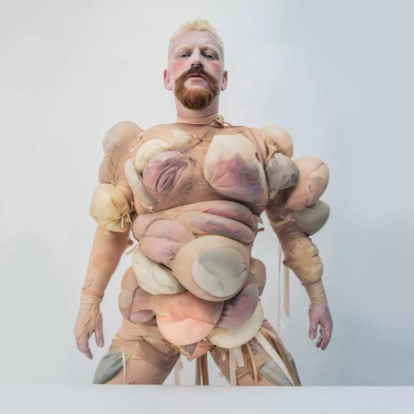Photo of artist Tom Rasmussen in a costume making them look like a body builder made of tights. 