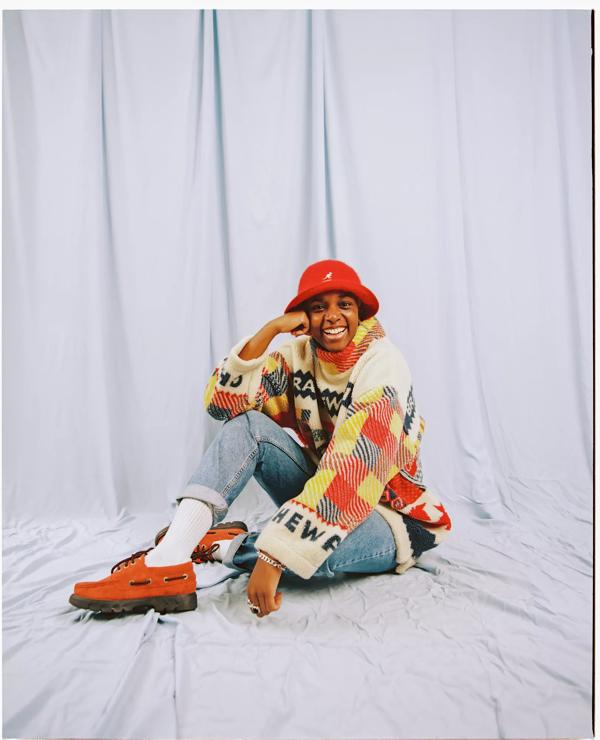A person sitting on the floor, wearing a red bucket hat and checked jumper