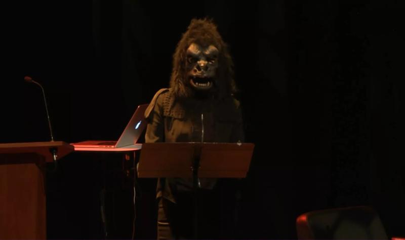 A member of Guerilla Girls on stage at the 2013 Meltdown Festival; she wears a guerilla costume whilst standing at a lectern
