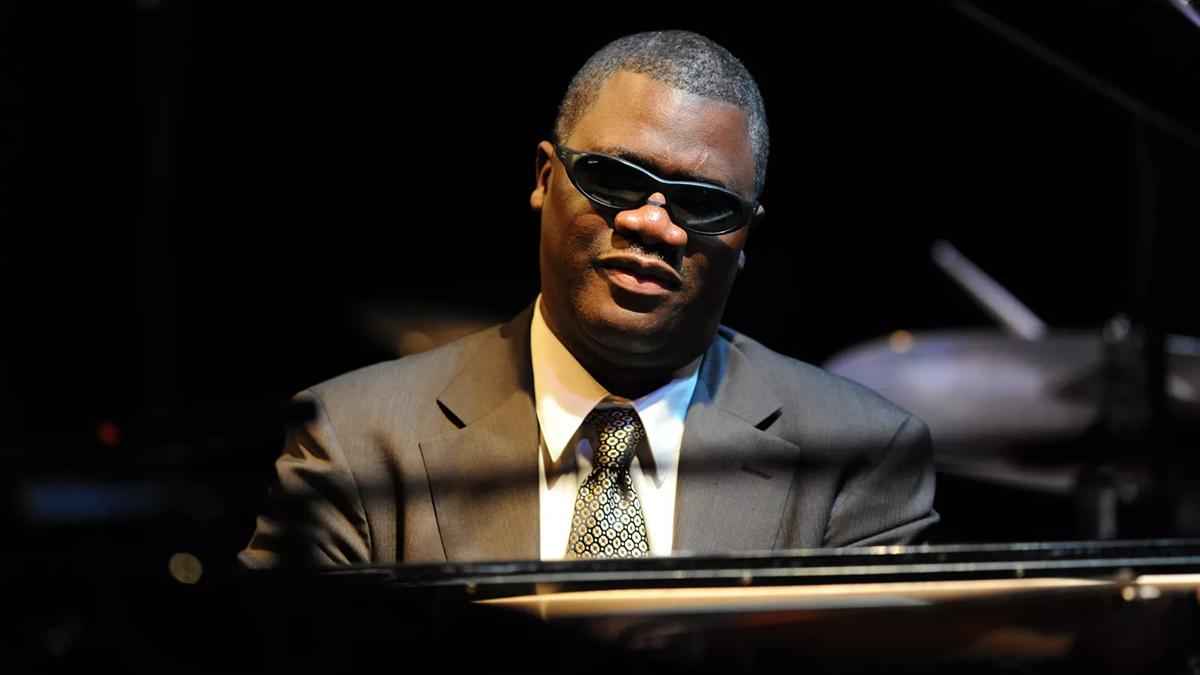 Marcus Roberts playing the piano, in a suit and tie and dark glasses