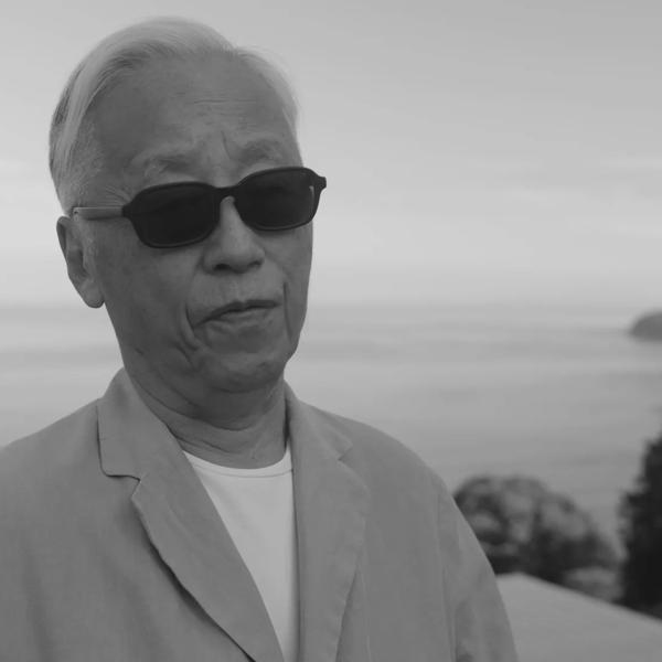 Hiroshi Sugimoto, an older Japanese man, wears sunglasses and a light jacket whilst being interviewed overlooking his Enoura Observatory in Japan