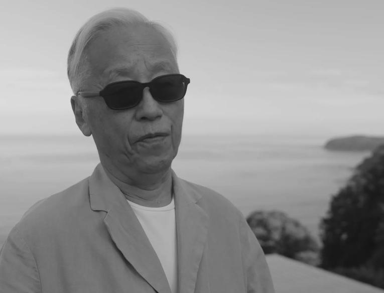 Hiroshi Sugimoto, an older Japanese man, wears sunglasses and a light jacket whilst being interviewed overlooking his Enoura Observatory in Japan