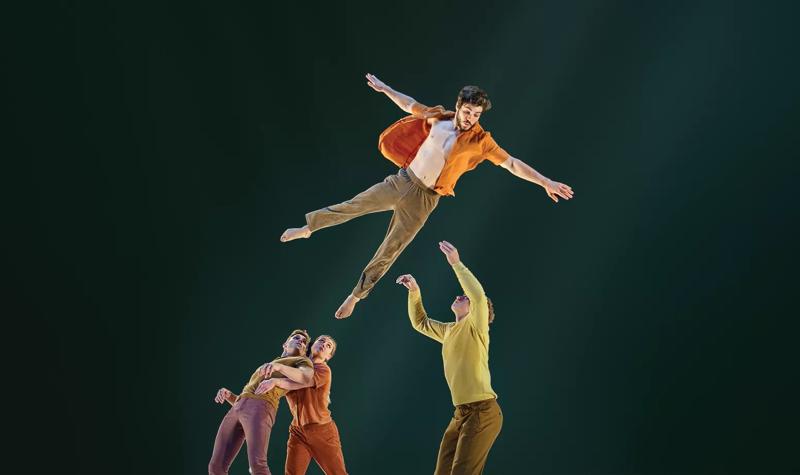 Four Circa acrobats performing, with three standing and looking up at the 4th who is in the air