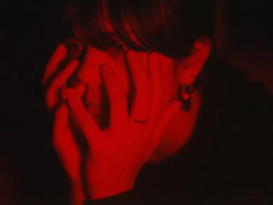 Red toned portrait of artist Bat For Lashes with her head in her hands. 