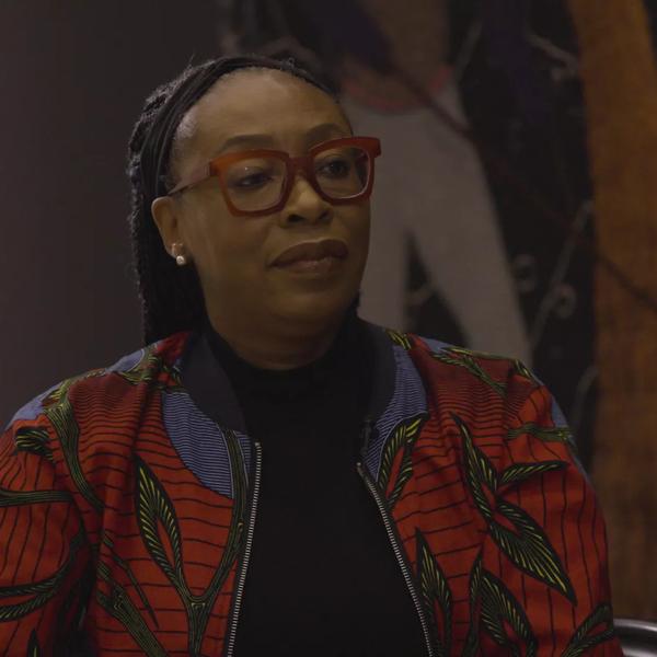 The artist Otobong Nkanga wearing red framed glasses and a multi-coloured jacket
