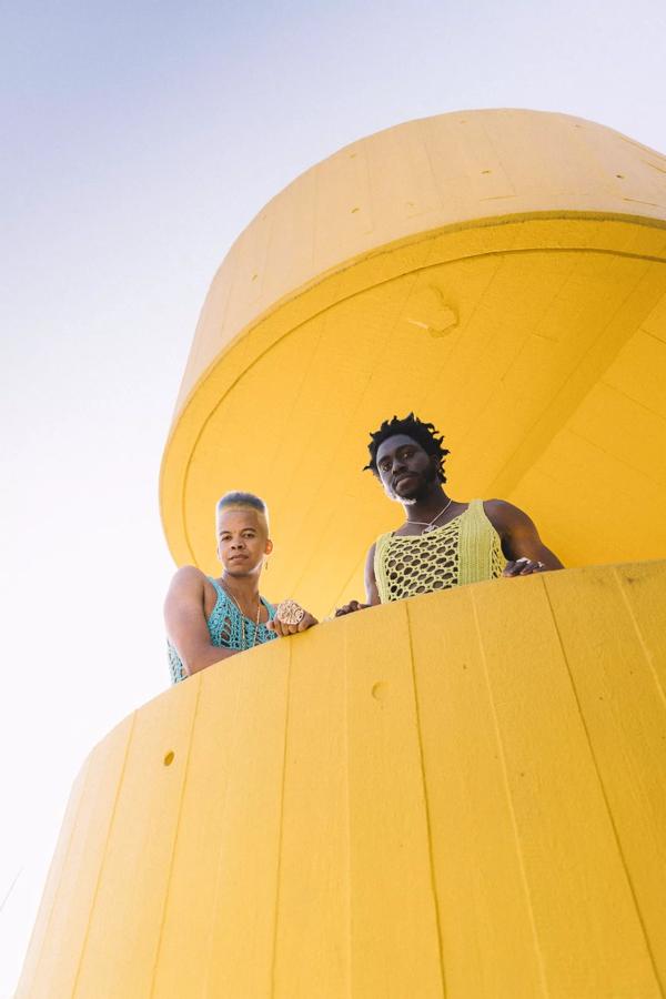 Two people stare down from a yellow spiral staircase