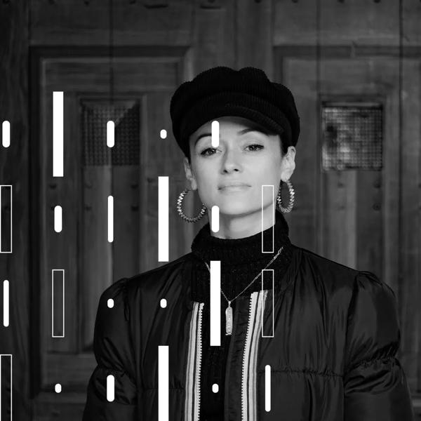 Portrait of writer Sabrina Mahfouz wearing gold earrings and a black hat