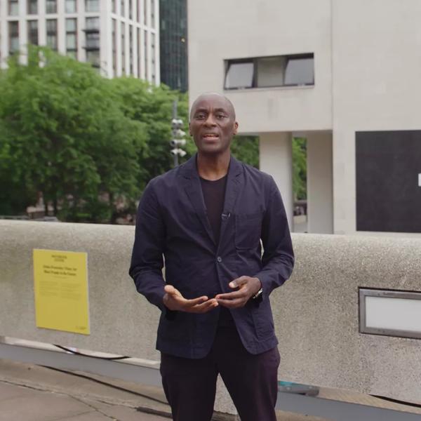 Curator Ekow Eshun stands outdoors at the Southbank Centre, behind him on the exterior wall of the Royal Festival Hall is Alisha B Wormsley's artwork 'There Are Black People in the Future'