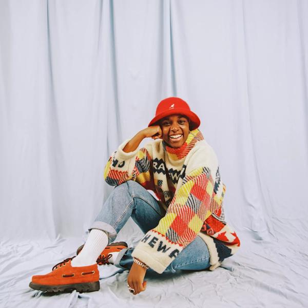 A person sitting on the floor, wearing a red bucket hat and checked jumper