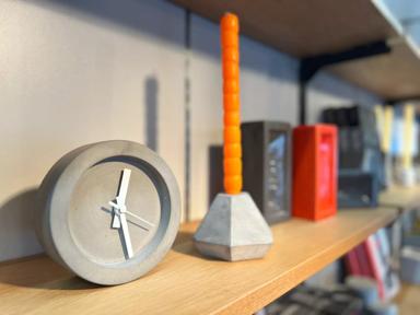 A grey concrete table clock with white hands and no numbers, sitting on a shelf in the Hayward Gallery Shop