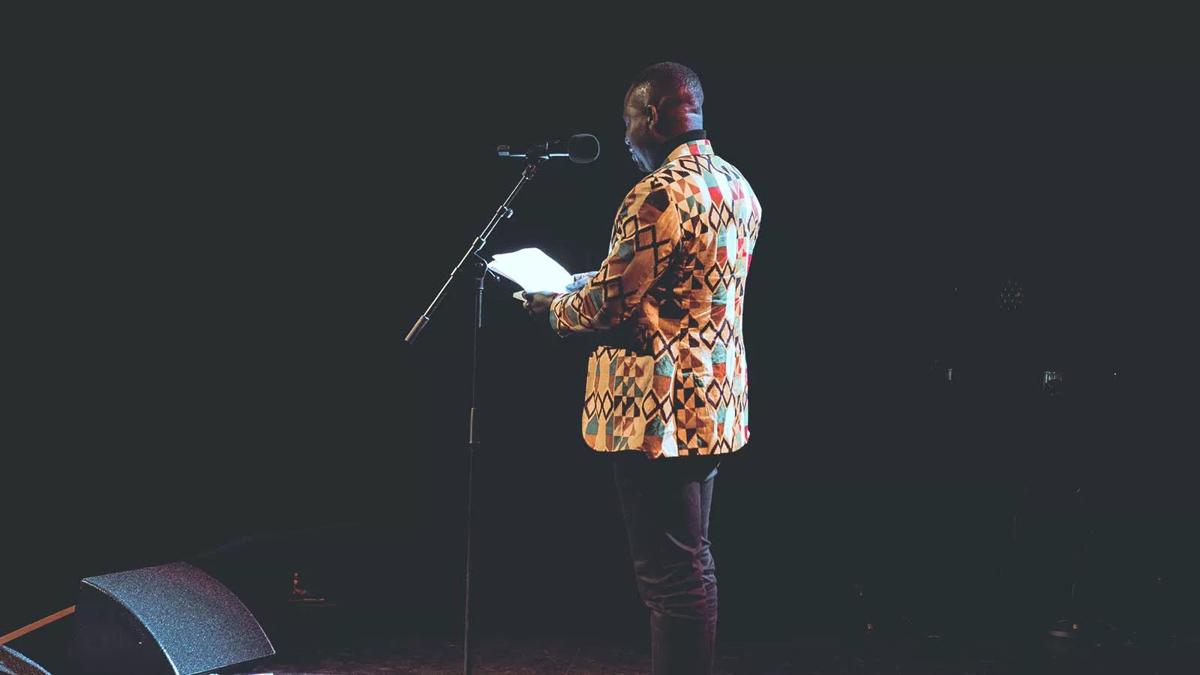 A poet stands at the microphone, performing at Out-Spoken