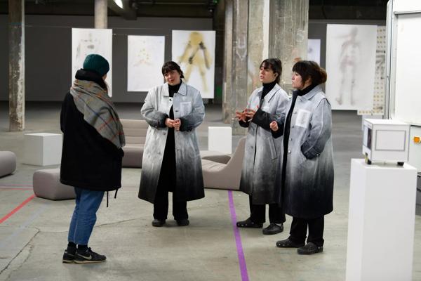 3 people wearing matching grey coats talking to another person 