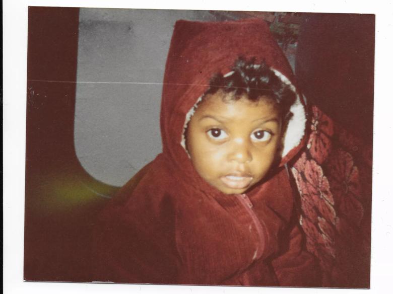 Image of Christopher Samuel aged 2 with a red corduroy jacket with a hood on. Sitting on the   back of a bus.