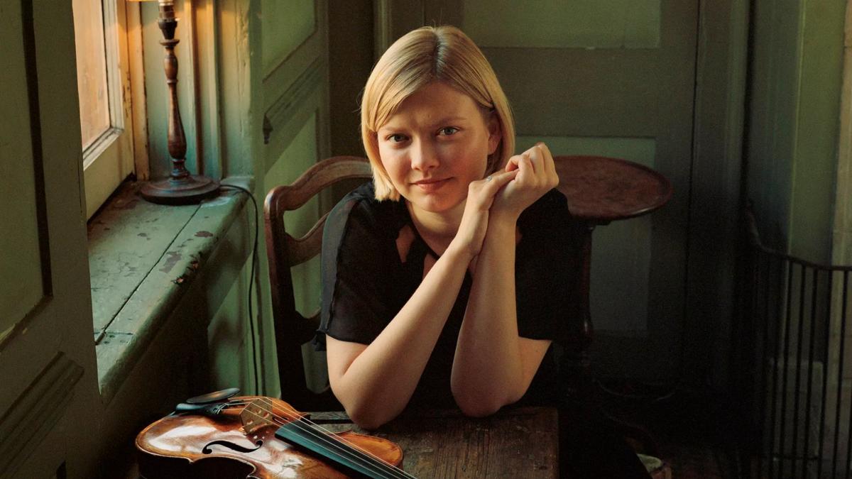 A woman with short, blonde hair sitting behind a table with a violin