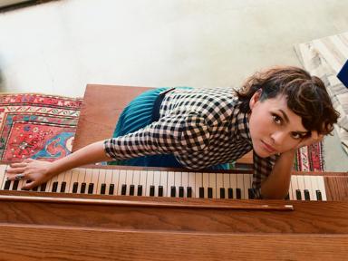 A musician sat a piano in a black and white gingham shirt