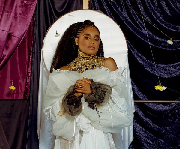 Roxanne Tataei wears all white and is depicted in the style of an 18th century painting against a dark curtained backdrop