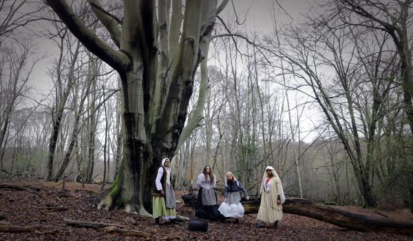 Four people standing in a forest wearing old fashioned peasant clothing.