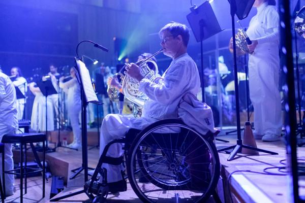 Paraorchestra: Trip the Light Fantastic at the Bristol Beacon. A person in a wheelchair plays the french horn.