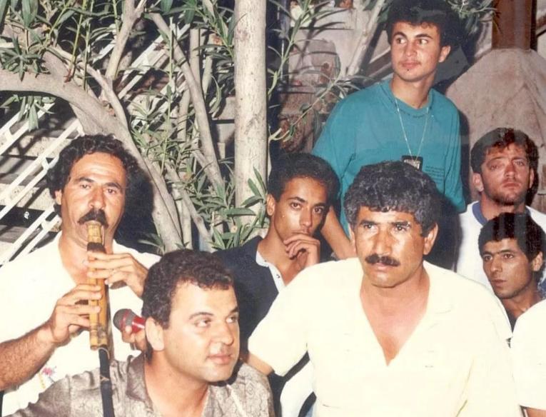 Group of men sat together one playing a wooden woodwind instrument and another holding a microphone